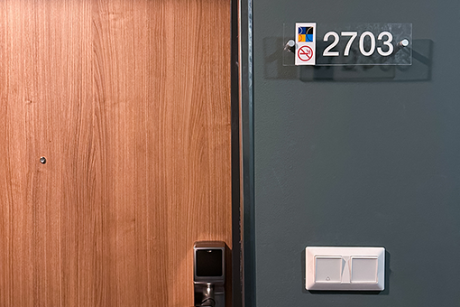 Szoba 2703 ajtaja kulcskártyás beléptető rendszerrel és világos fa borítással.